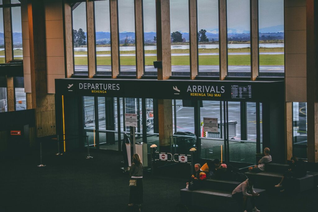 Busy airport terminal area with people, featuring departures and arrivals signs.